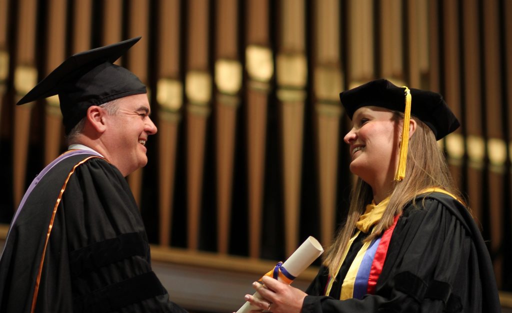 Jacques Nör hands a diploma to a graduating School of Dentistry postdoctoral student while they are both dressed in doctoral regalia during the 2024 School of Dentistry commencement ceremony. 