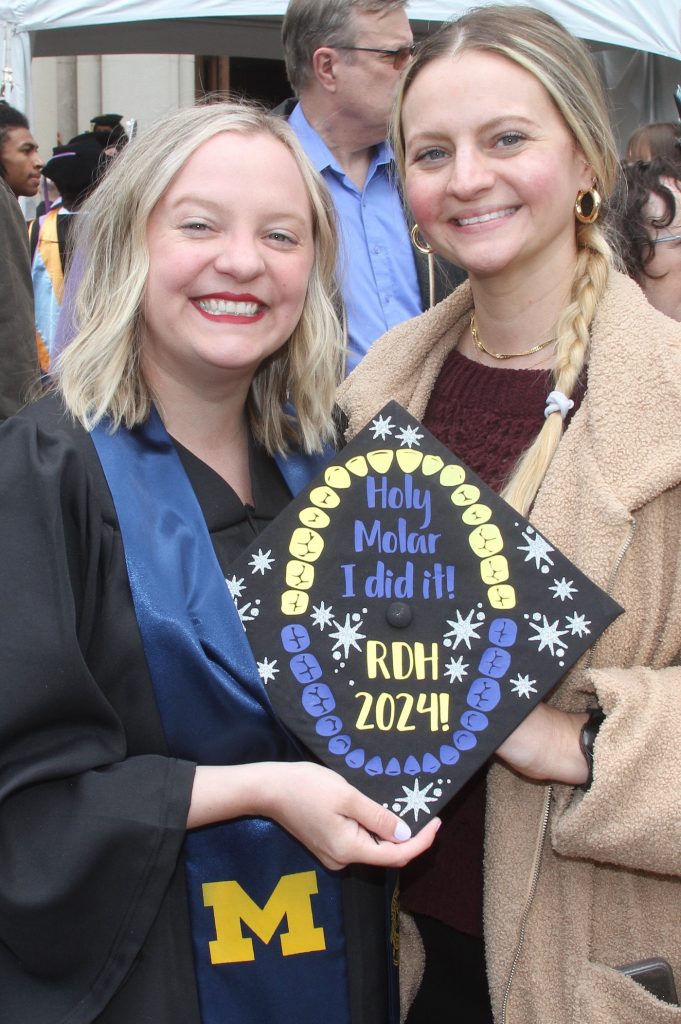 A graduated School of Dentistry Dental Hygiene wearing academic regalia holds a cap that reads 'Holy molar I did it! RDH 2024' and poses with her sister. 